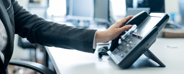 Close-up of a female employee's hand on a landline phone. Woman picks up a push-button telephone at...