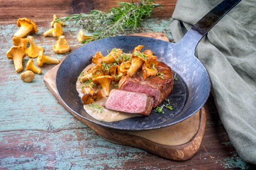 Gebratenes dry aged Wagyu Roastbeef Steak mit Pfifferlingen in Rahmsauce angeboten als close-up in einer rustikalen schmiedeeisernen Pfanne
