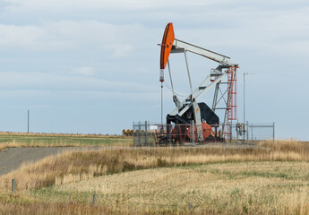 Fototapeta na wymiar Oil well pump jack in a rural Alberta famer's field. Oil production, job creation, and economic recovery concept. Fossil fuels industry and natural resources 