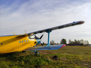 Yellow and blue old biplane plane with a single piston engine and propeller against a blue sky with clouds on the airfield with green grass in summer