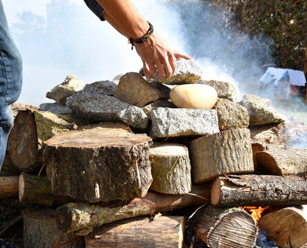 Hands leaving stones called grandmothers on the firewood for the temazcal.