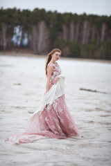 Fototapeta na wymiar beautiful red-haired girl in a pink dress walks on the seashore, fabulous photo session