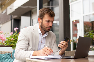Fototapeta premium The young businessman is working online, and writing in his notebook in the coffee bar 