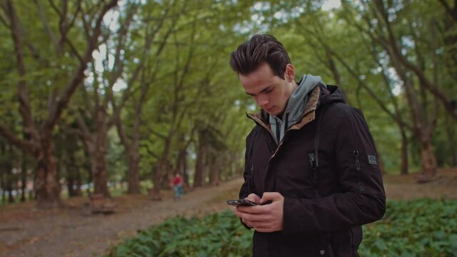 Hipster Man sending voice messages with mobile phone at park, teenager student use audio message search on grass in park, backpacker walking tour