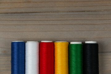 Hilos de colores para costura,, azul, blanco, rojo, amarillo, verde, negro con un fondo de madera 