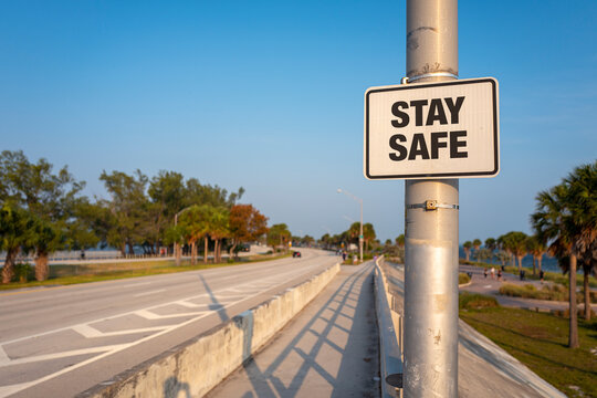 "STAY SAFE" - Close-up of a road street sign message agains a South Florida road and walking pathway surrounded by palm trees and other tropical vegetation