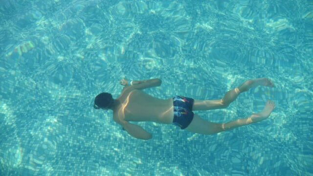 Buoyant boy diving and swimming underwater in a paddling pool in slow motion