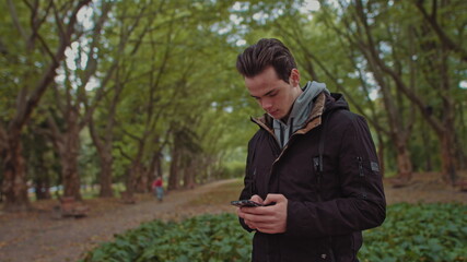 Hipster Man sending voice messages with mobile phone at park, teenager student use audio message search on grass in park, backpacker walking tour, voice search
