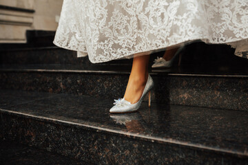 Bride in white dress and elegant shoes on marble stairs. Legs of the bride in white shoes.