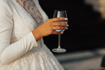 Elegant bride with a glass of white wine in her hand. Ring on her finger. She is engaged. Cropped shot, close up.