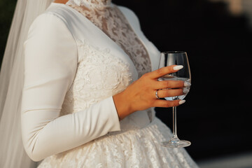 Cropped shot of bride with luxury white dress holding a glass of wine. Ring on her finger, she is engaged.