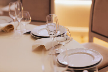 Table setting with white plates, glasses and napkins on beige table. Empty plates and glasses.
