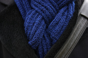 Deep blue knitted scarf on the background of black men's coat. Autumn cold weather. October.