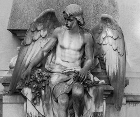 Fototapeta na wymiar Sculpture of a stone winged angel on a tomb in cemetery. Selective focus