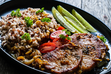 Roasted meat, buckwheat and pickled cucumbers on wooden table
