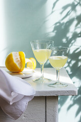 Italian liqueur limoncello in crystal glasses and ripe lemons on a wooden table.