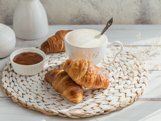 Delicious breakfast with fresh croissants and cup of coffee served with jam on a white wooden background. Delicious Baking