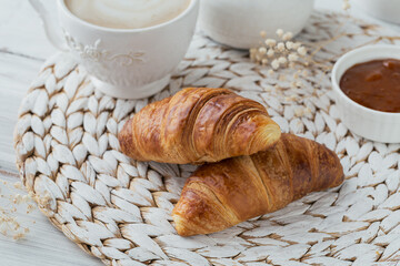Delicious breakfast with fresh croissants and cup of coffee served with jam on a white wooden background. Delicious Baking