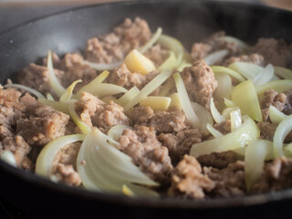 Pork nuggets frying in pan with white onion
