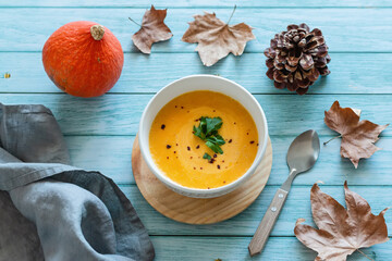 Pumpkin cream soup with dry leaves and cones on blue table top, lifestyle culinary background