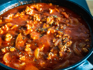 Pork nuggets frying in pan with tomato sauce and white onion