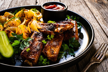 Tasty roasted ribs with baked potatoes vegetables on wooden table
