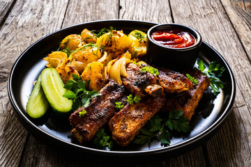 Tasty roasted ribs with baked potatoes vegetables on wooden table
