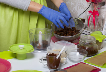 A woman in gloves puts dates in a blender to make candy. Cooking candies from dried fruits and nuts at home in self-isolation during an epidemic.