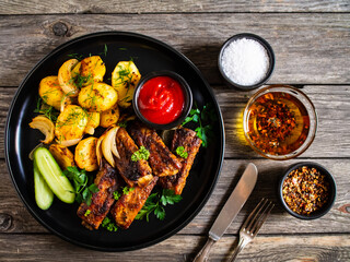 Tasty roasted ribs with baked potatoes vegetables on wooden table
