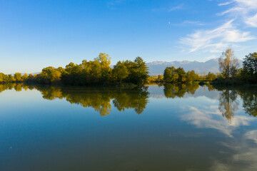Lake at the edge of the mountains with forest reflected in the clear water. Idyllic autumn landscape. The forest and the sky in the reflection of the water. Quiet autumn fishing landscape