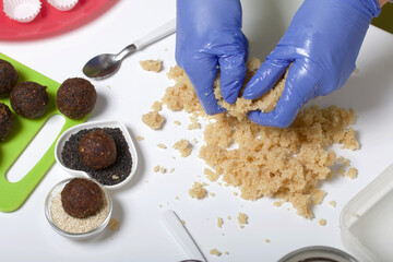 A woman mixes a mass of almonds. Dried fruit and nut sweets. Made at home in self-isolation during the epidemic. They lie on black and white sesame seeds.
