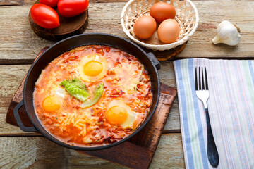 israeli fried eggs shakshuka with cheese in a frying pan next to a fork and a napkin.