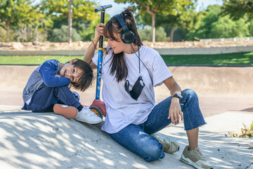 mother and son sitting on the ramp of a skate park in a very affectionate way next to the child's scooter