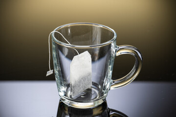 Brew black tea from a sausage bag in a transparent mug with reflection on a gradient background