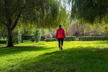 Back view of a young fitness a woman walks a red jacket in the sunny summer season park