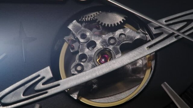 Metallic second arrow passing by gears in planet shape on open balance on luxury swiss watch. Open mechanism on black clock face. Dramatically ight flicking. Extreme closeup, real time shot