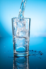 Clear ice water in transparent glass with reflection on blue gradient background