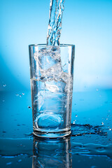 Clear ice water in transparent glass with reflection on blue gradient background