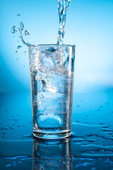 Clear ice water in transparent glass with reflection on blue gradient background