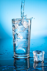 Clear ice water in transparent glass with reflection on blue gradient background