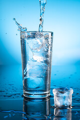 Clear ice water in transparent glass with reflection on blue gradient background