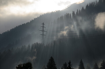 Power line pylon of power grid in misty forest with fog on a beautiful morning in the Swiss alps.