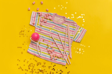 T-shirt, pink rattle and sweets on yellow background