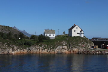 Fototapeta na wymiar Bodo / Norway - June 15 2019: Lonely traditional white houses on the rocks in the harbor of Bodo
