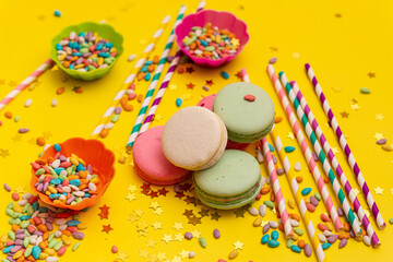 Fototapeta na wymiar Multi-colored macaroons and sweets on yellow background. Baby birthday concept