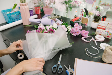 Top view of florist making flower bouquet on wooden surface.Florist at work: pretty young woman making bouquet of flowers.