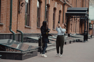 Fototapeta na wymiar Young female photographer strolling along alley with girlfriend. Travelers walk in the city. Look attractions city.