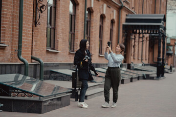 Young female photographer strolling along alley with girlfriend. Travelers walk in the city. Look attractions city.