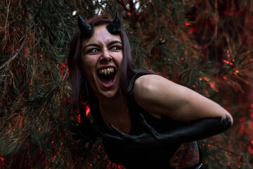 a girl with fangs and horns obsessed with evil screams in the burning forest. Halloween occultism,...