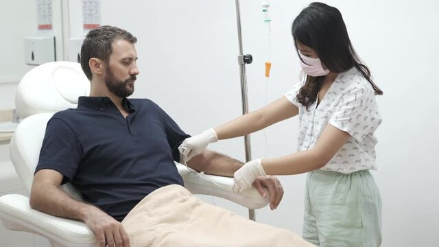 Nurse or doctor preparing and adjusting infusion for young man patient in hospital or beauty salon. Healthcare, wellness and medicine concept